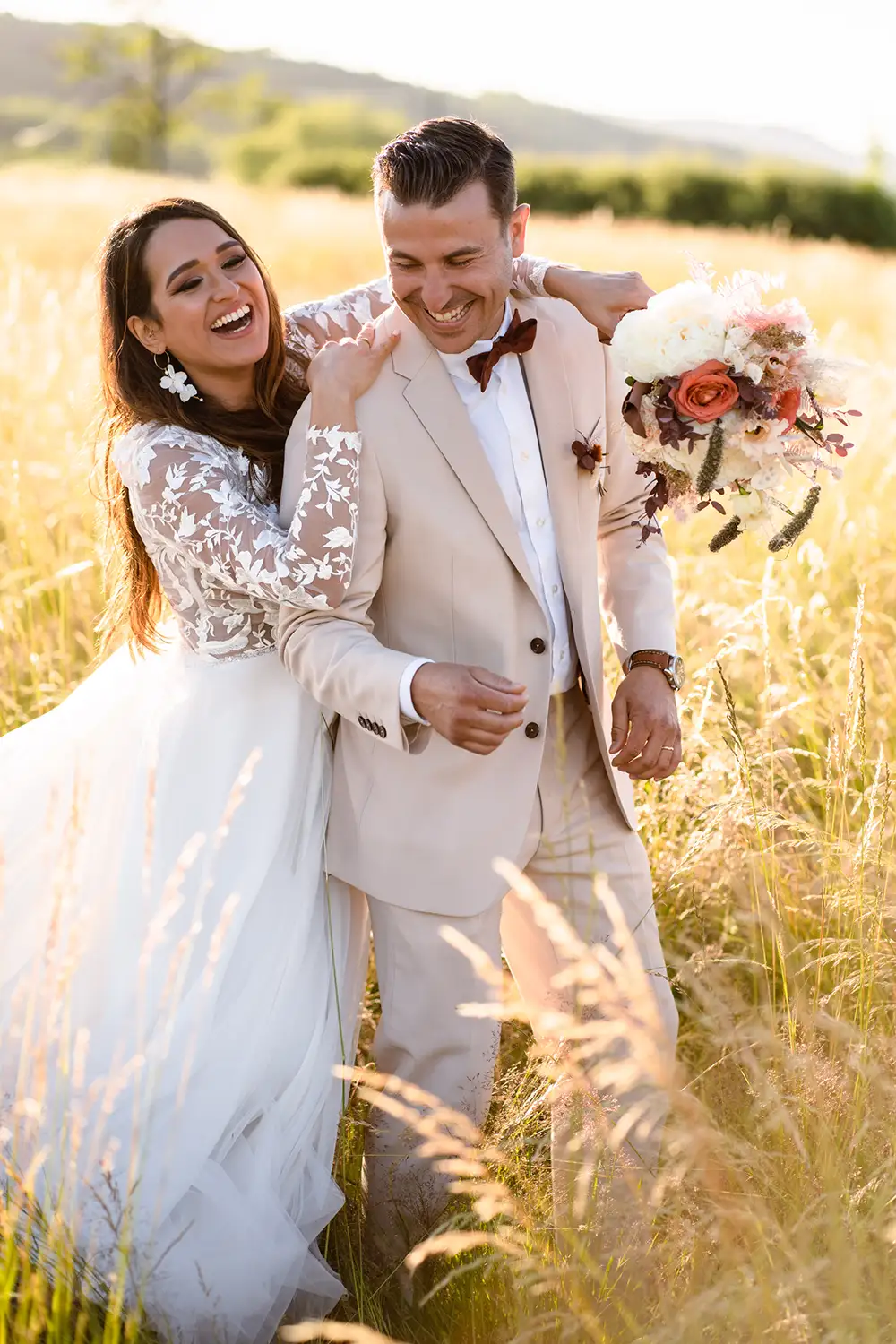 Un couple de mariés riait dans le champ des hautes herbes.