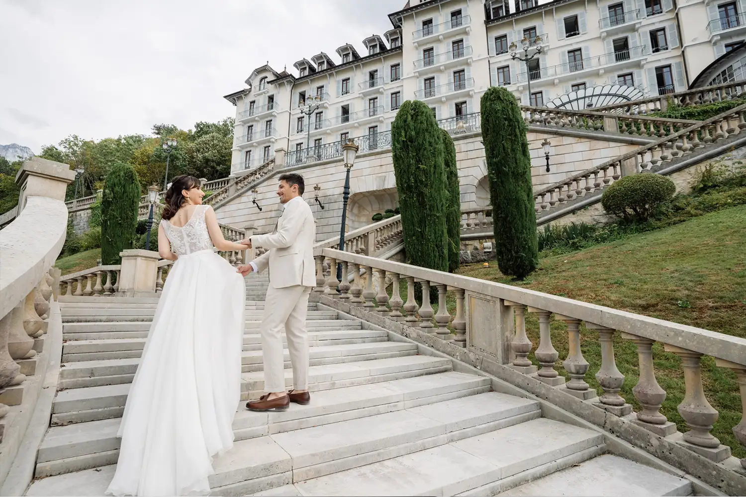 Les mariés montent les escaliers et sourirent du Palace de Menthon